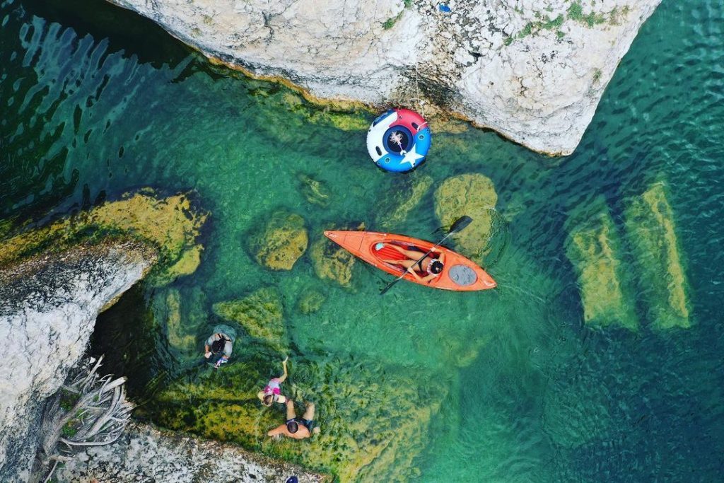 Aerial view of a serene river with kayakers and swimmers enjoying the clear, turquoise waters surrounded by rocky cliffs in Uvalde County, Texas