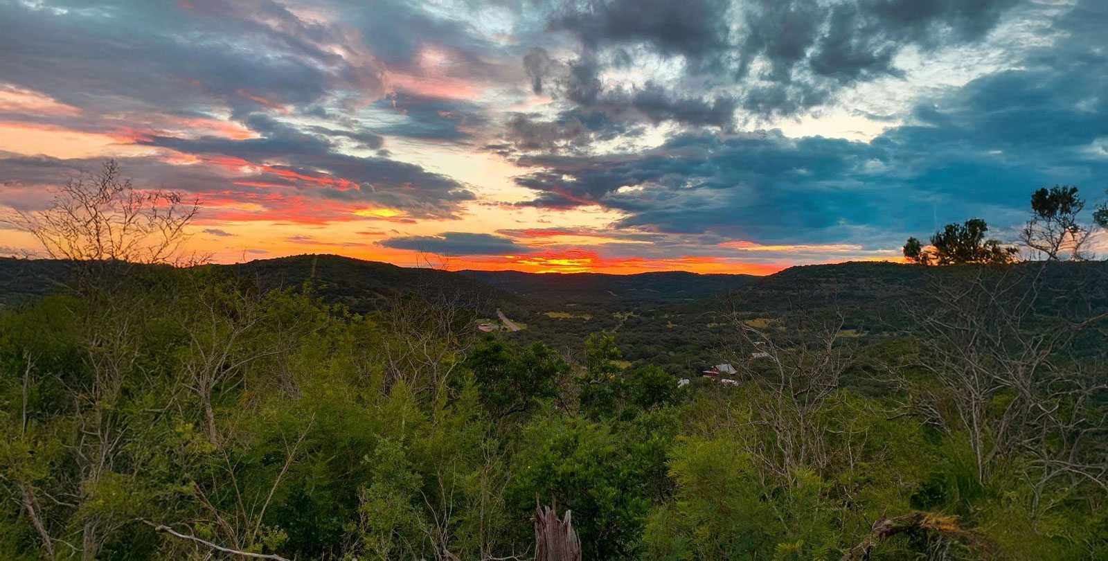 A breathtaking sunset paints the sky with hues of orange and pink over rolling hills and lush green forests in Uvalde County, Texas in Uvalde County, Texas
