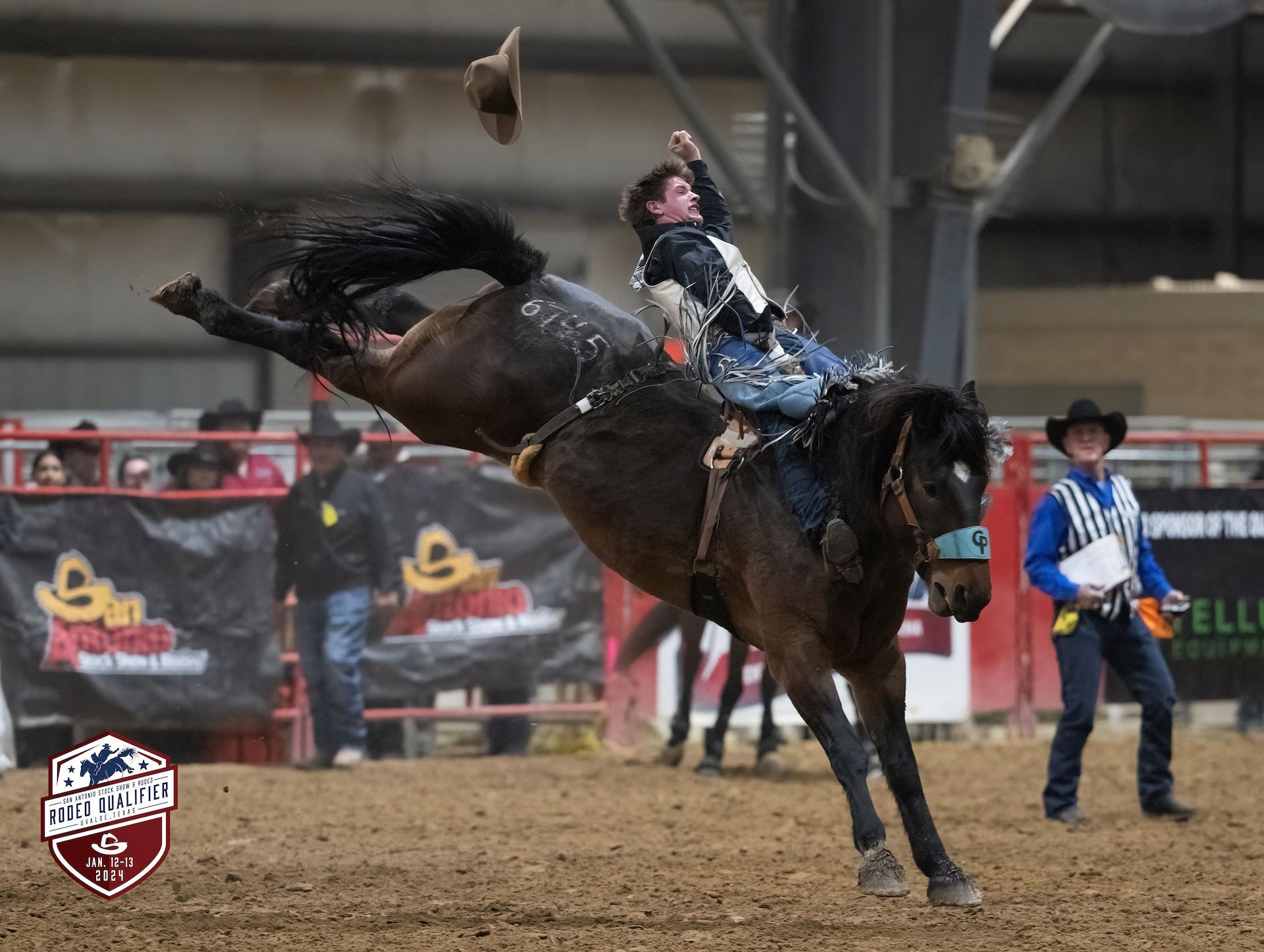 A cowboy is dramatically thrown from a bucking bronco during a rodeo event, with the horse's front legs off the ground and the cowboy's hat flying through the air in Uvalde County, Texas