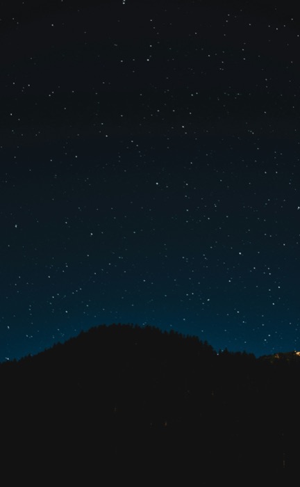 A dark, starry night sky stretches over a silhouetted mountain range in Uvalde County, Texas in Uvalde County, Texas