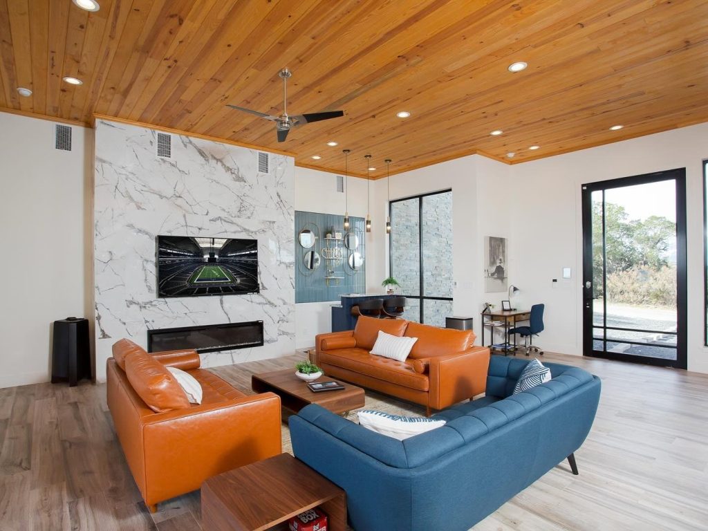 A modern living room with a wooden ceiling, marble fireplace, and orange and blue leather furniture in Uvalde County, Texas
