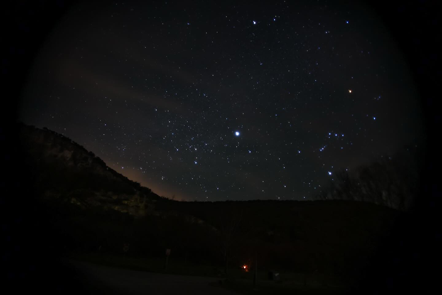 A breathtaking night sky filled with countless stars, including a prominent constellation, over a dark, hilly landscape in Uvalde County, Texas
