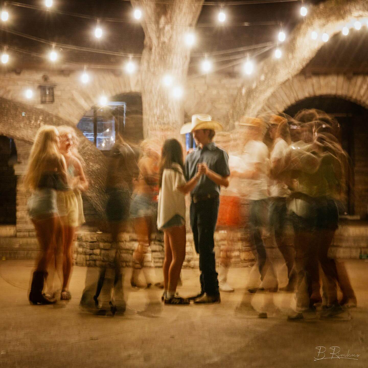 A lively country dance under string lights with a cowboy and his partner at the center in Uvalde County, Texas