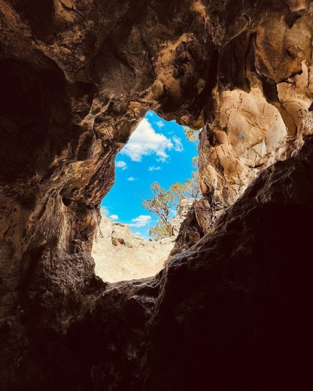 A natural rock archway frames a vibrant blue sky with scattered clouds, creating a serene and picturesque scene in Uvalde County, Texas