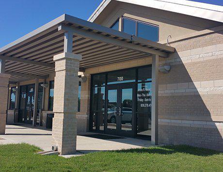 A modern building with a covered entrance and large glass doors, set against a clear blue sky in Uvalde County, Texas