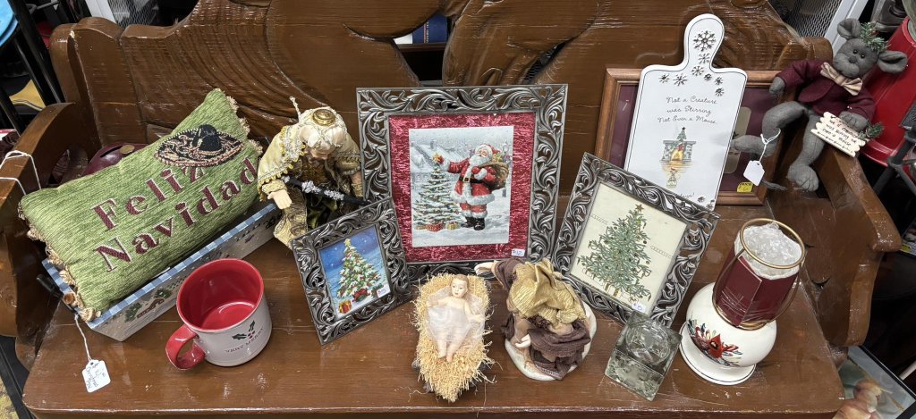 A festive display featuring a variety of Christmas-themed items arranged on a wooden bench, including framed artwork, a mug, and decorative figurines in Uvalde County, Texas