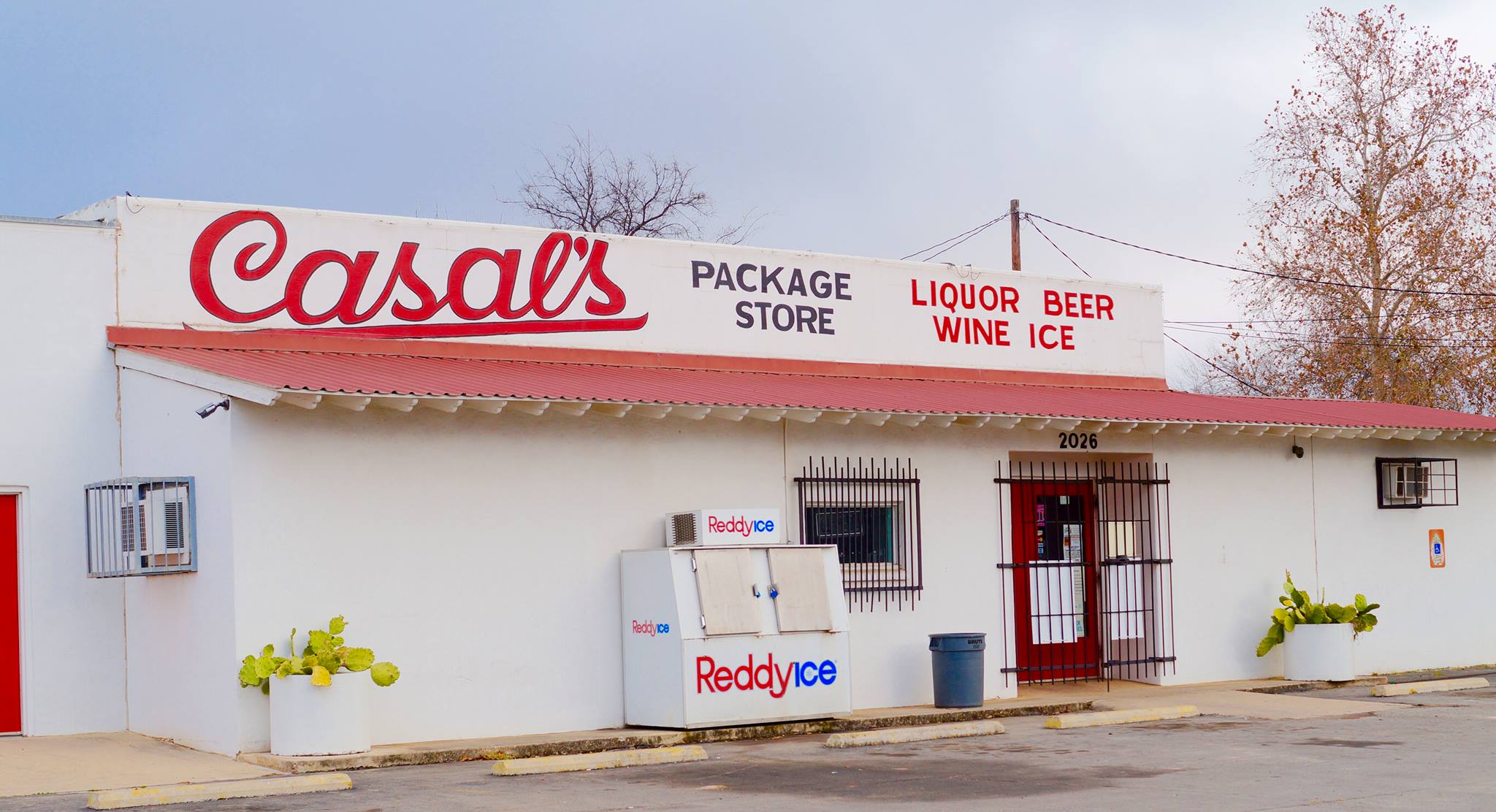 Casals Package Store, a white building with a red roof, features a large sign advertising liquor, beer, wine, and ice in Uvalde County, Texas