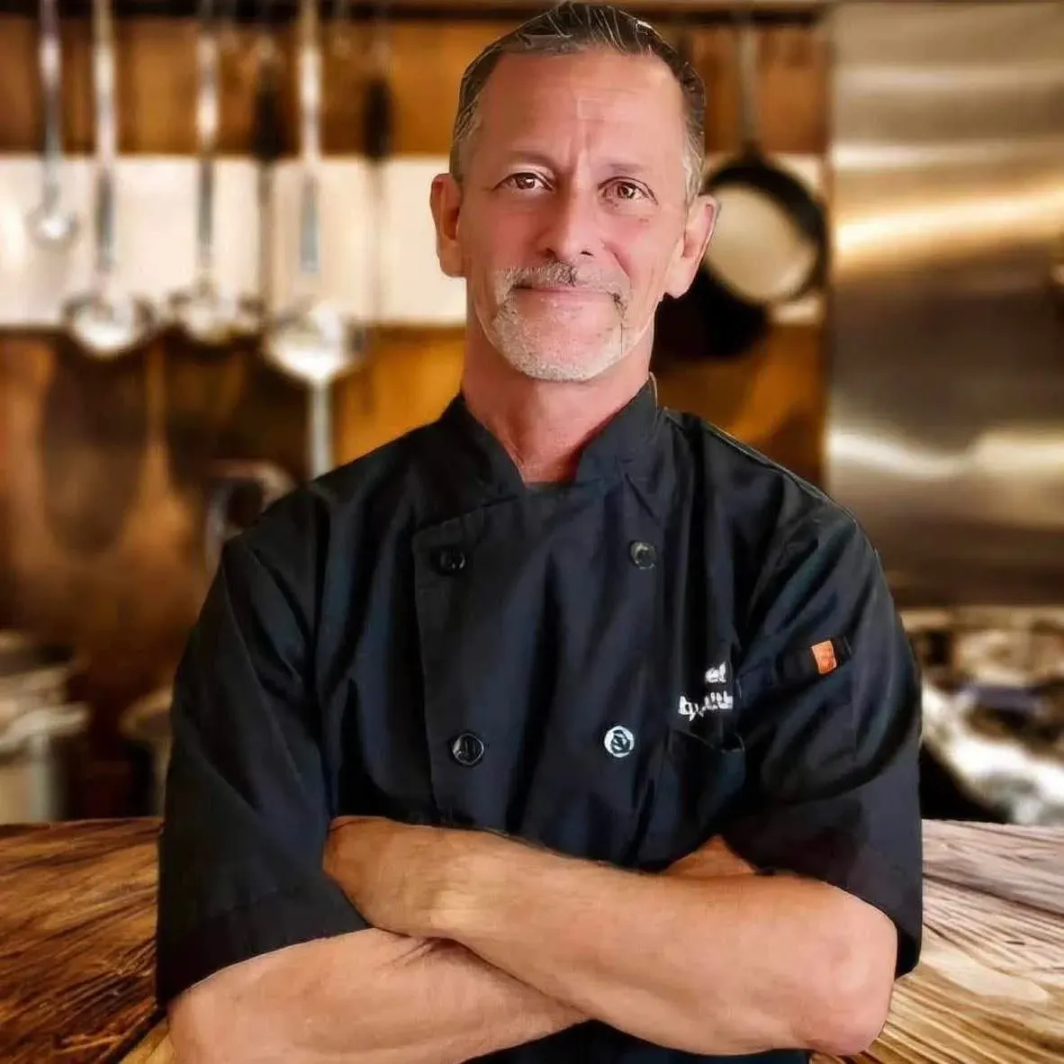 A confident chef stands with arms crossed in a professional kitchen in Uvalde County, Texas