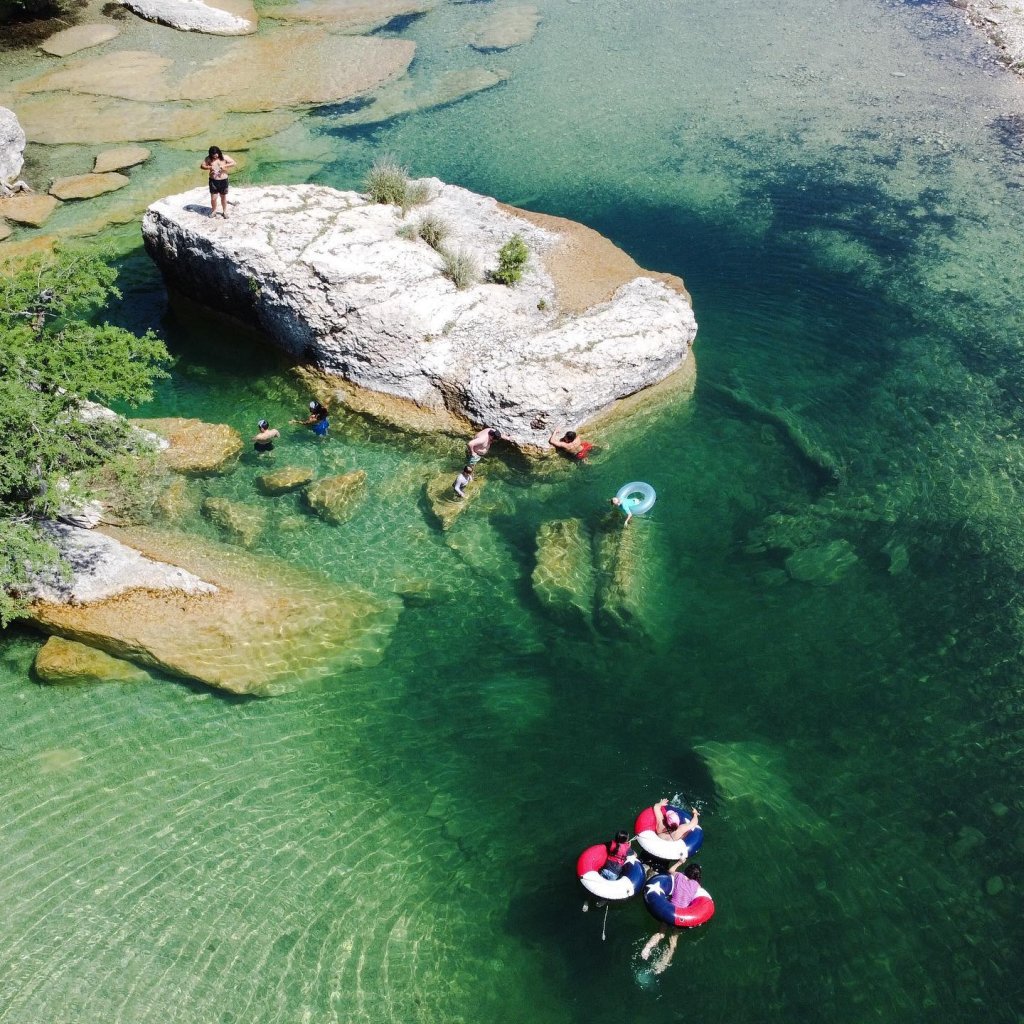 Aerial view of a crystal-clear river with swimmers and floaters enjoying the water around large rocks and small islands in Uvalde County, Texas