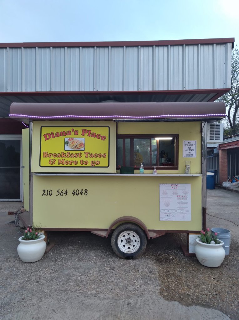 A bright yellow food truck named Diana's Place serves breakfast tacos and more, parked outside a building with a metal roof in Uvalde County, Texas