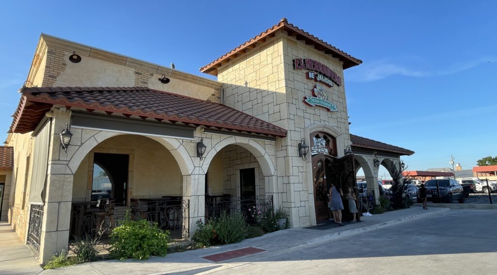 A charming Mediterranean-style restaurant with arched entrances and a tiled roof, set against a clear blue sky in Uvalde County, Texas