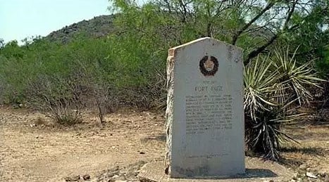 A weathered stone monument stands amidst desert vegetation, commemorating the history of Fort Inge in Uvalde County, Texas in Uvalde County, Texas