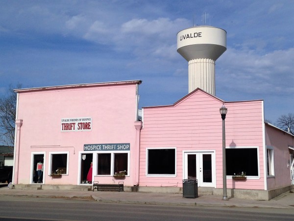A pink thrift store with a water tower labeled 'UVALDE' in the background in Uvalde County, Texas