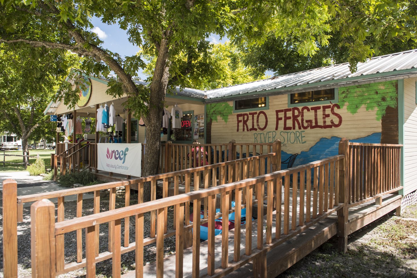 A quaint outdoor store named 'Frio Fergus' with a colorful mural and a wooden ramp leading to the entrance, surrounded by lush greenery in Uvalde County, Texas