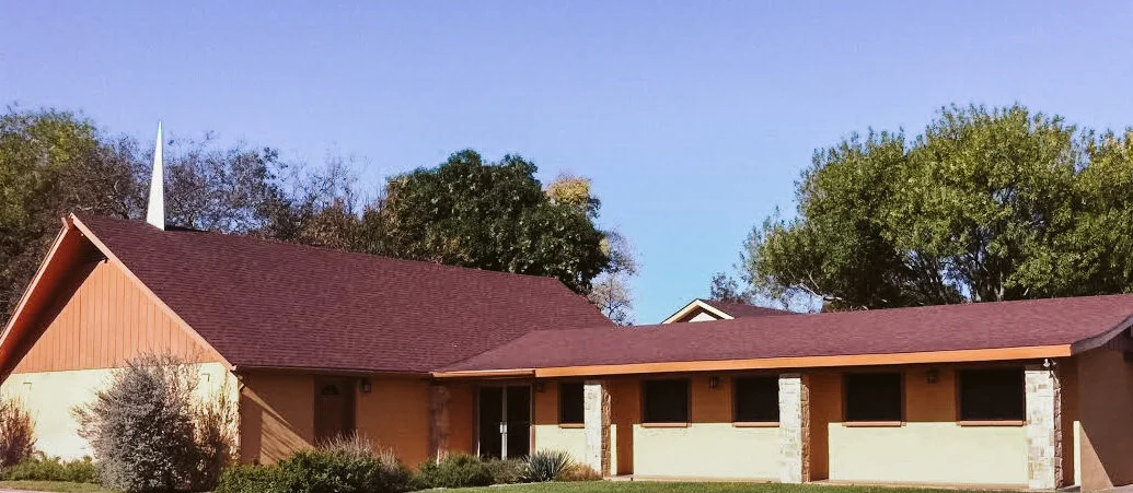A church with a red roof and a white steeple is surrounded by lush green trees and a well-maintained lawn in Uvalde County, Texas