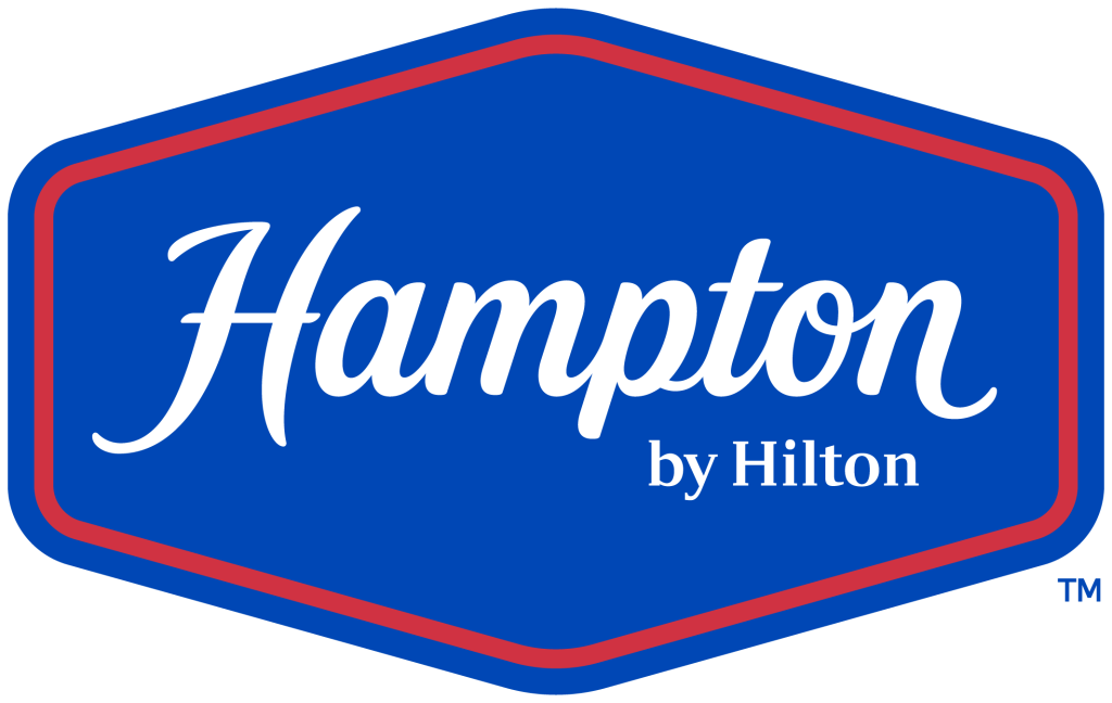 The Hampton by Hilton logo features a blue hexagonal shape with a pink outline, containing the brand name in elegant white script in Uvalde County, Texas
