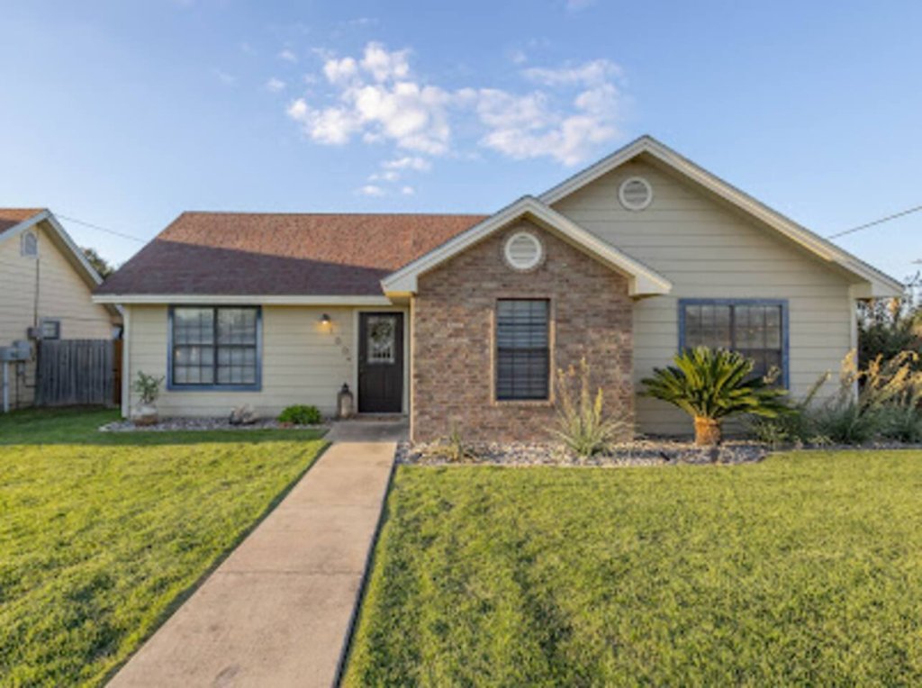 A charming single-story home with a brick facade and a well-maintained lawn, featuring a covered entry and a side driveway in Uvalde County, Texas