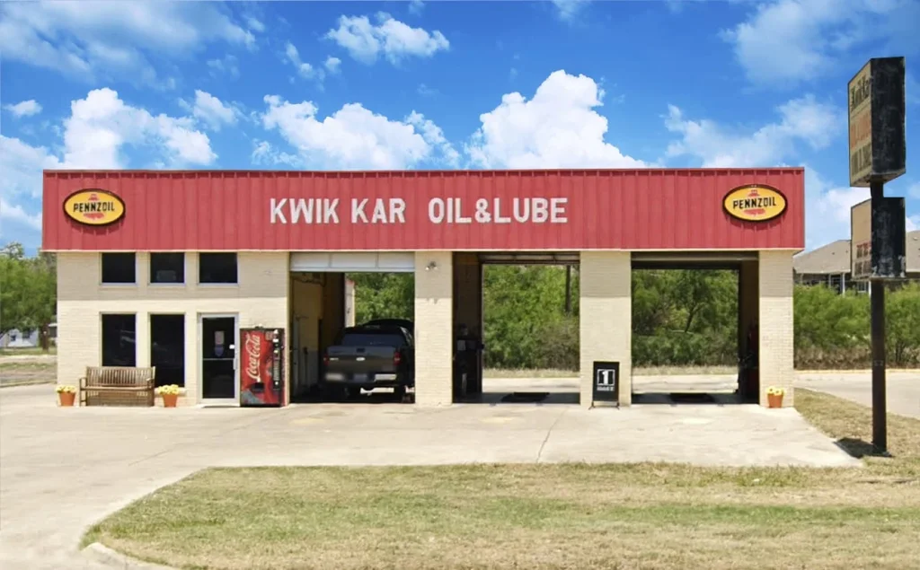 A red and white Kwik Kar Oil & Lube auto service center with three open bays and a sign advertising oil changes for $19.99 in Uvalde County, Texas