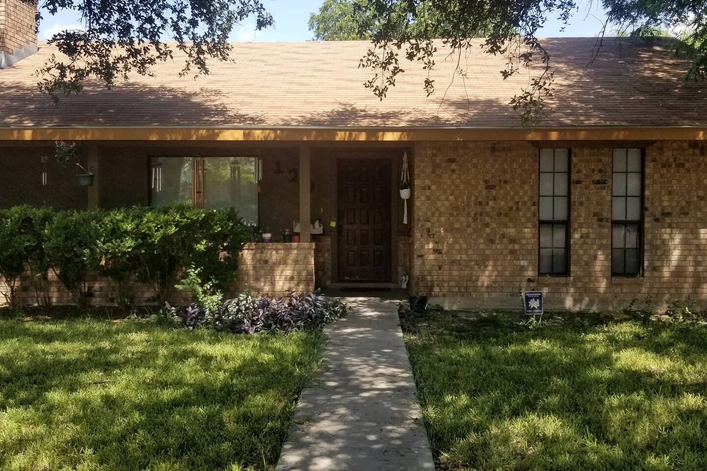 A single-story brick house with a covered front porch, surrounded by a well-maintained lawn and garden in Uvalde County, Texas