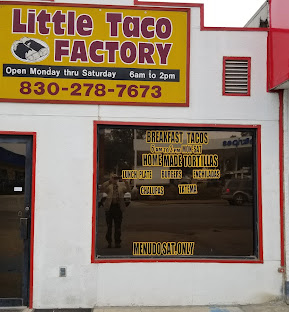 A man stands in front of a window displaying the menu for Little Taco Factory, which offers breakfast tacos and homemade Mexican dishes in Uvalde County, Texas