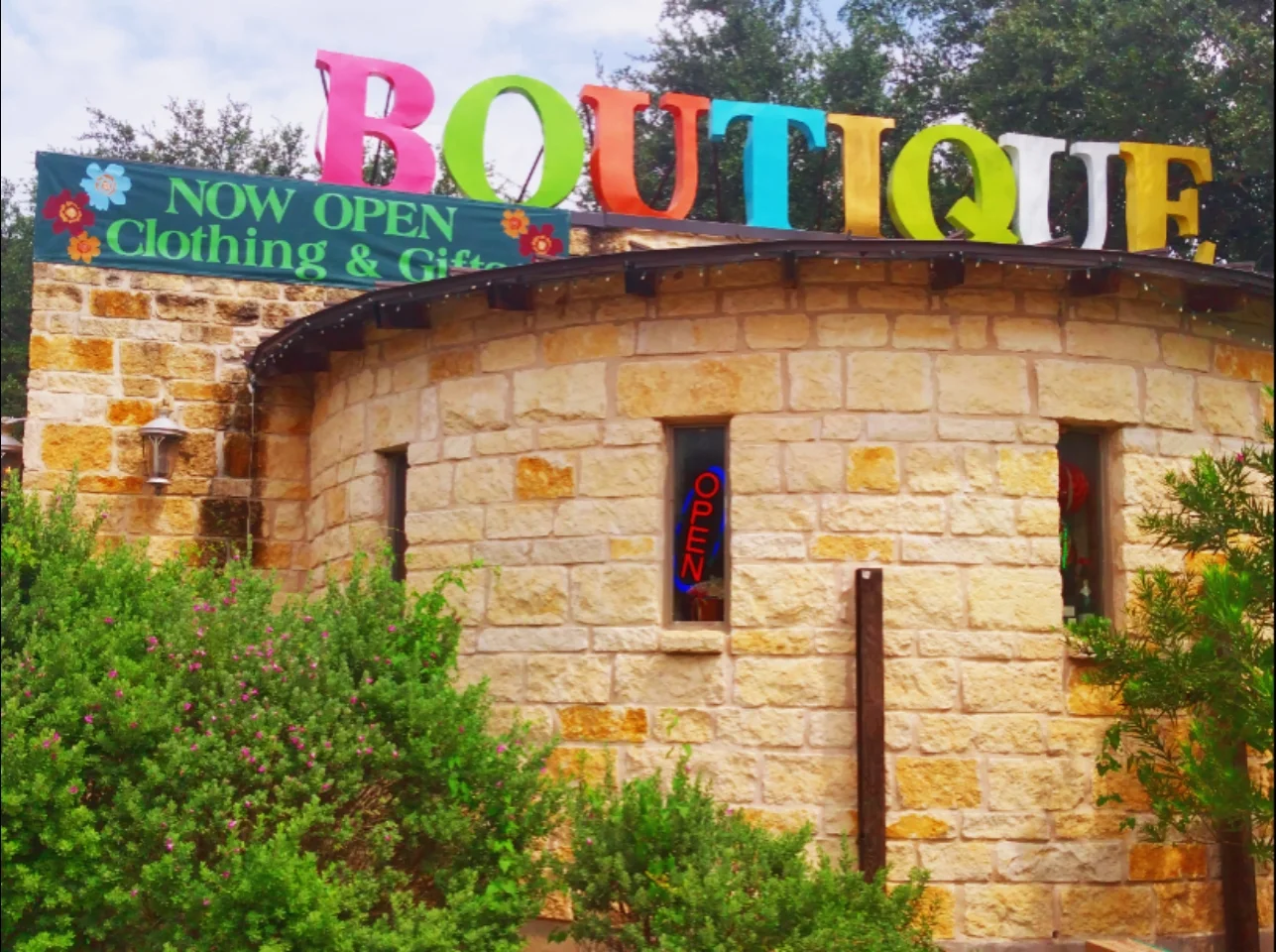 A charming stone building with a colorful sign reading 'Boutique' in large, playful letters, advertising clothing and gifts in Uvalde County, Texas