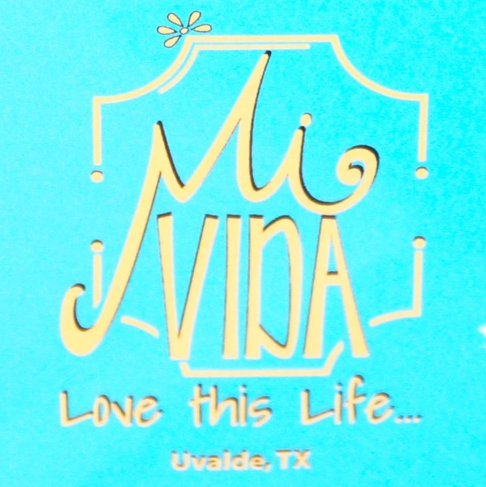 A blue sign with gold lettering reading 'Mi Vida: Love this Life... Uvalde, TX' in Uvalde County, Texas
