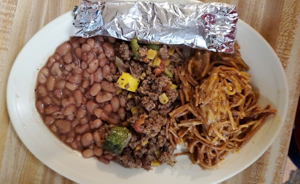 A hearty plate of Tex-Mex cuisine featuring refried beans, seasoned ground beef with vegetables, and a side of spaghetti with a creamy sauce, all served on a white plate in Uvalde County, Texas