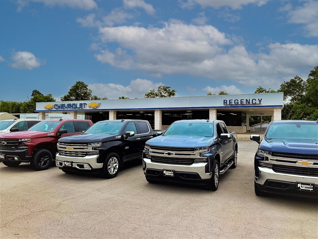 A row of five Chevrolet pickup trucks parked in front of a dealership with a blue sky and clouds in the background in Uvalde County, Texas