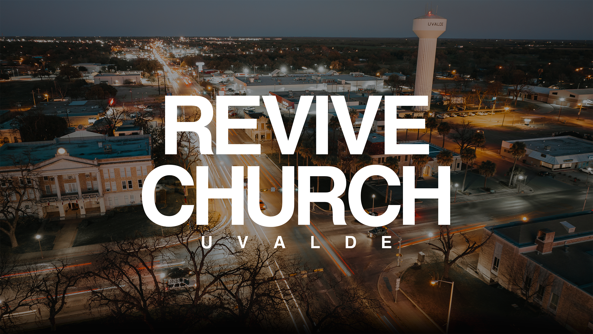Aerial view of a cityscape at dusk with a prominent church and water tower, Revive Church Uvalde in Uvalde County, Texas