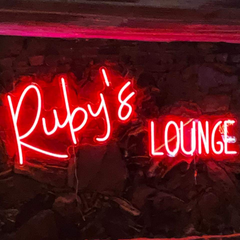 Ruby's Lounge neon sign with red and pink lights on a stone wall in Uvalde County, Texas