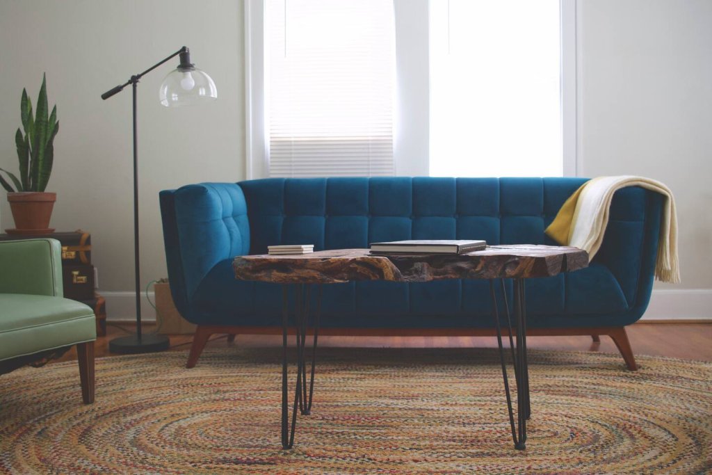 A cozy living room features a plush blue velvet sofa, a rustic coffee table, and a green armchair, all arranged on a circular jute rug in Uvalde County, Texas