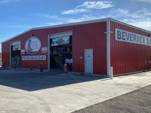 A large red metal building with a sign reading 'Beverage Barn' and a logo for 'Southern Door Experience' above the entrance in Uvalde County, Texas