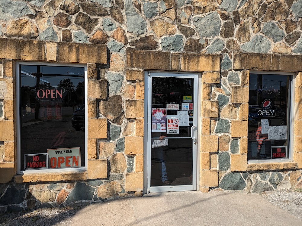 A rustic stone building with a glass door and windows, featuring signs that read 'OPEN' and 'WE'RE OPEN' in bright red letters in Uvalde County, Texas