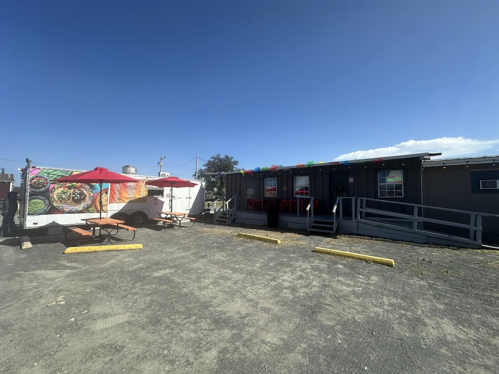 A food truck park with colorful trailers, outdoor seating, and a clear blue sky in Uvalde County, Texas