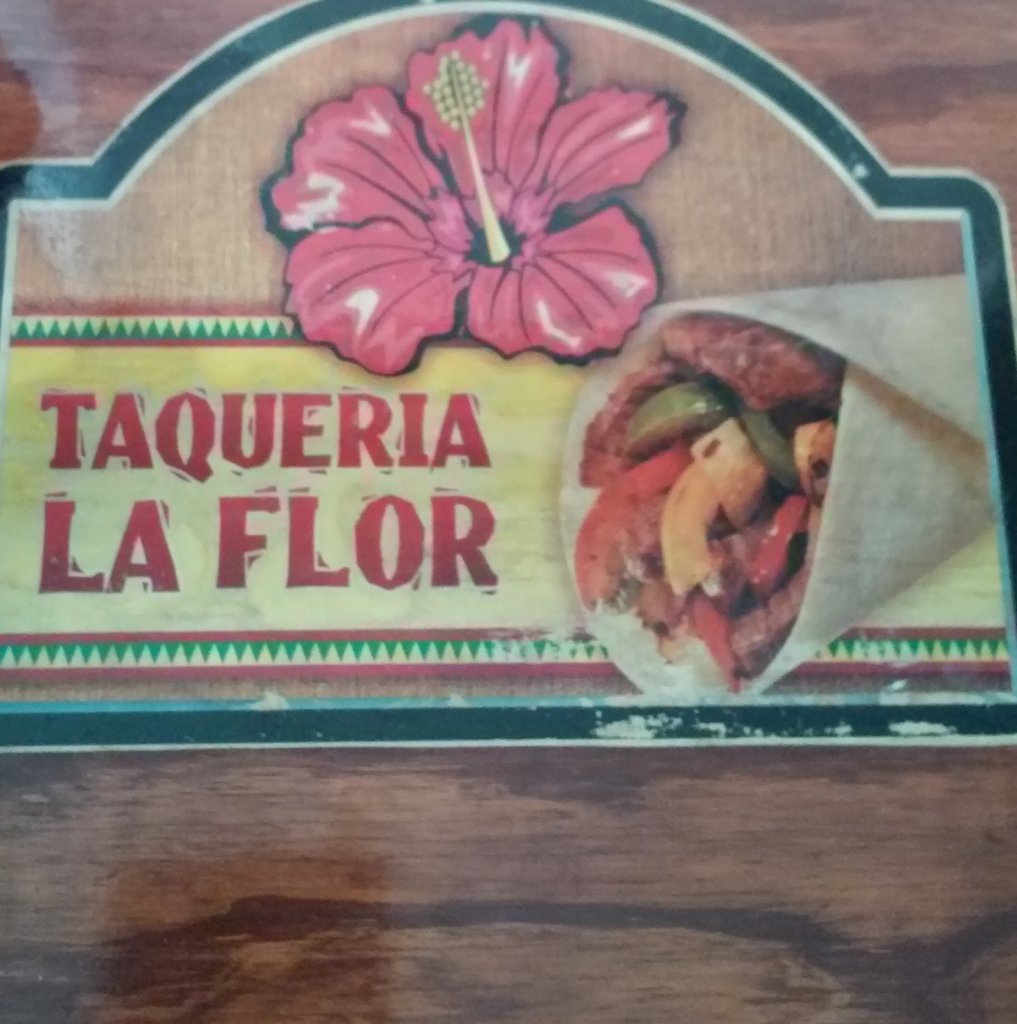 A colorful sign for Taqueria La Flor features a vibrant red hibiscus flower and a delicious-looking taco in Uvalde County, Texas