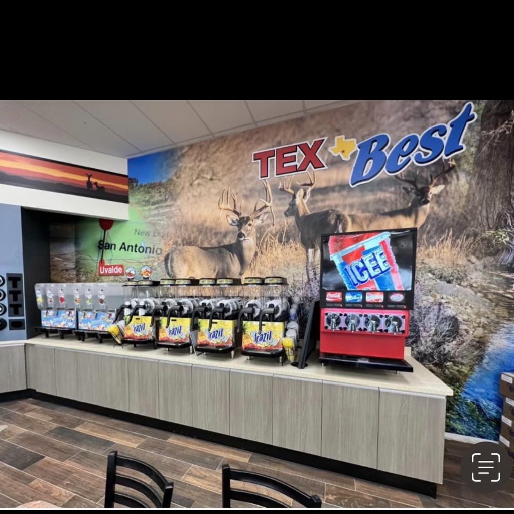 A convenience store counter with ice cream machines and a large mural of deer in a Texas landscape in Uvalde County, Texas