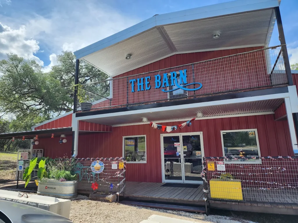 A charming red barn-style building with a blue sign reading 'The Barn' and a covered porch area in Uvalde County, Texas