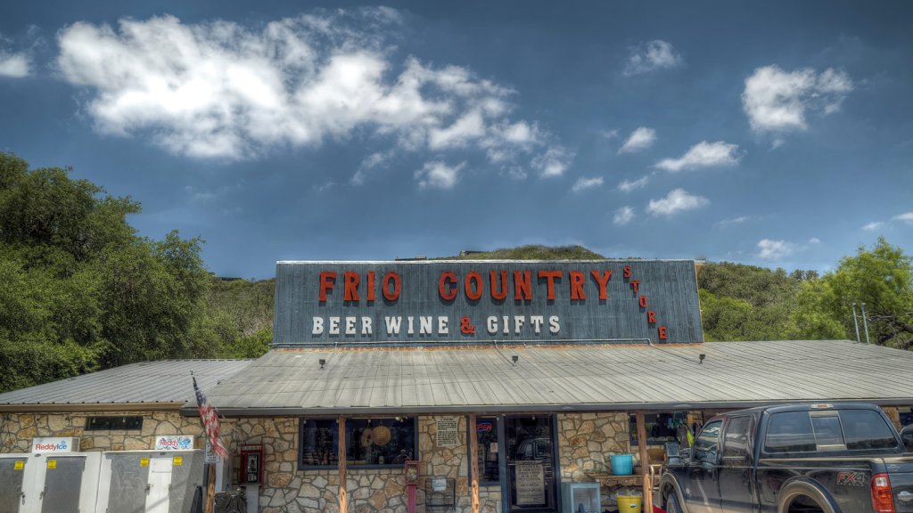 A quaint stone building with a sign reading 'Frio Country Beer Wine & Gifts' sits nestled among lush green trees in a picturesque Texas hill country setting in Uvalde County, Texas