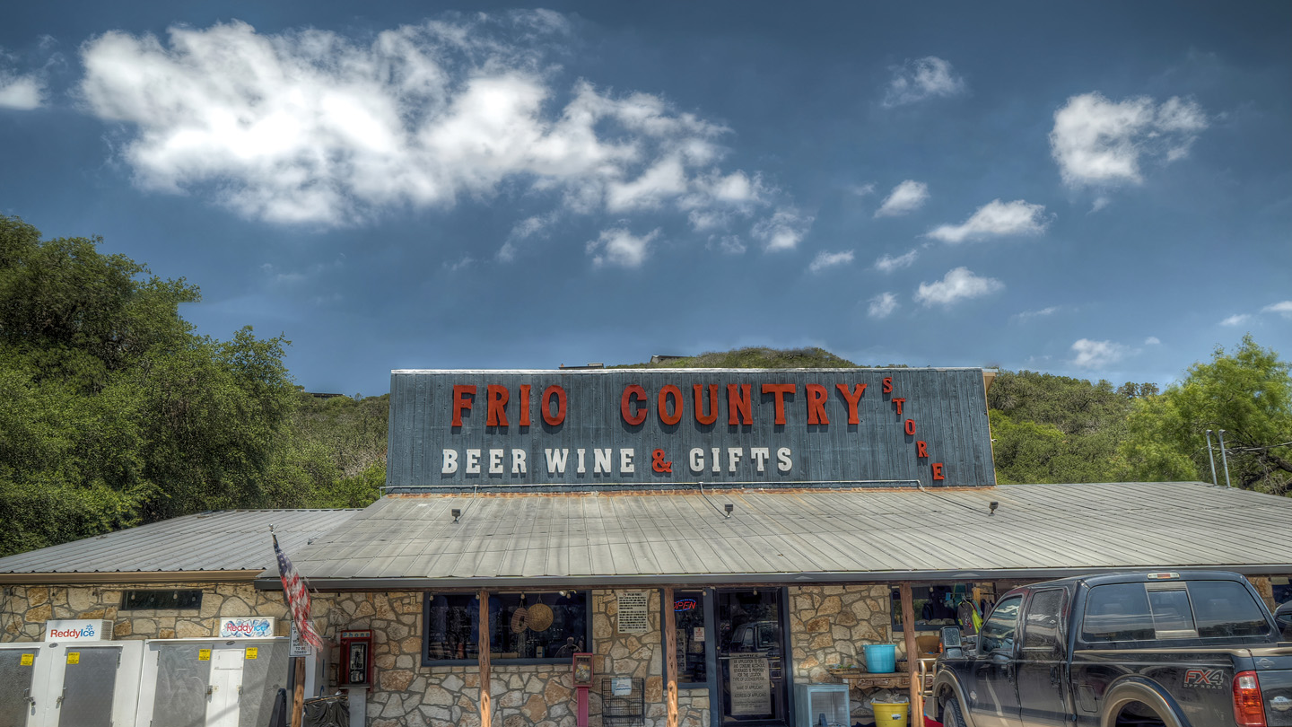 A quaint stone building with a sign reading 'Frio Country Beer Wine & Gifts' sits nestled among lush green trees in a picturesque Texas hill country setting in Uvalde County, Texas