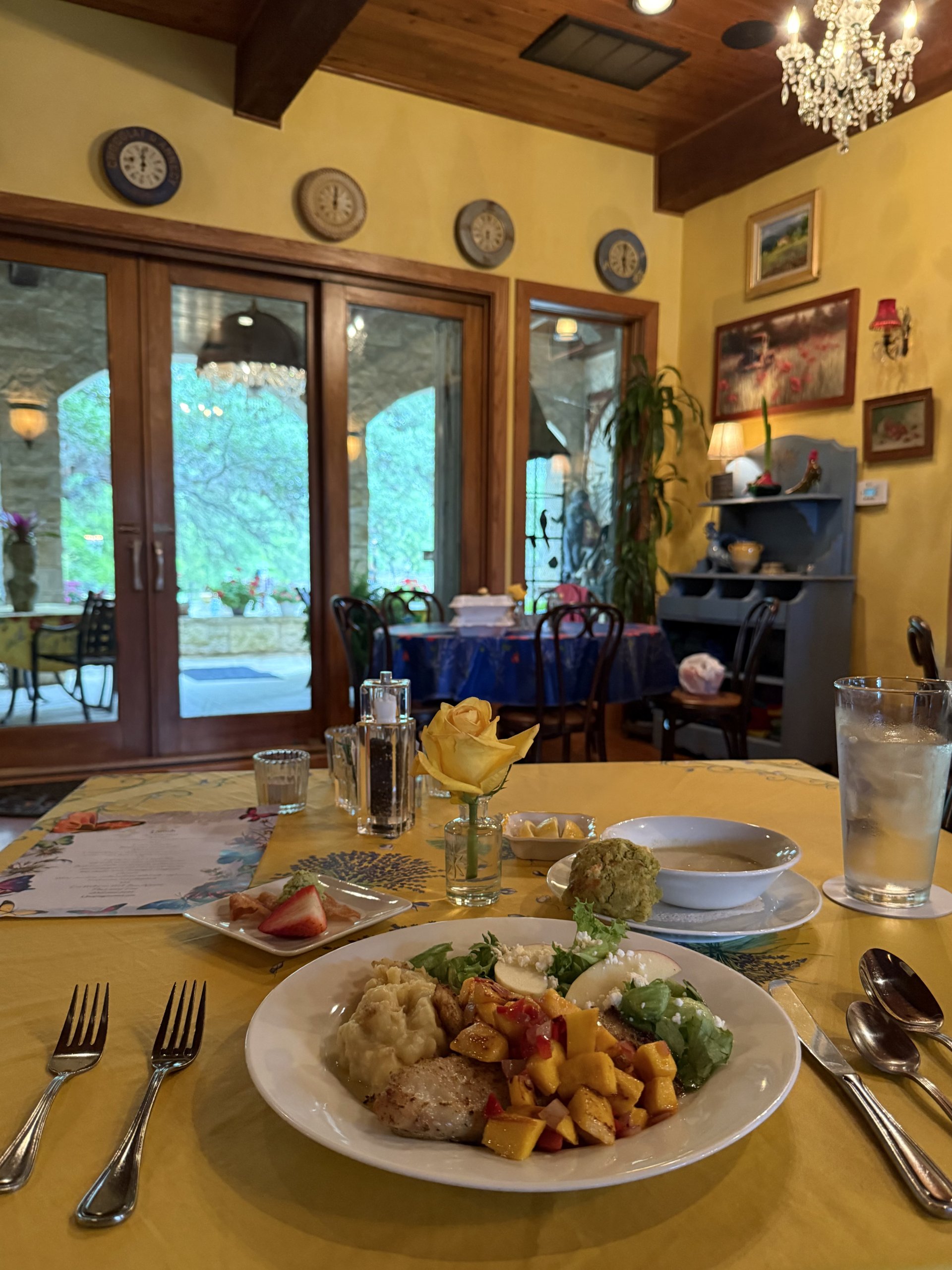 A beautifully set dining table with a variety of dishes, including a salad, soup, and main course, accompanied by elegant tableware and a yellow rose centerpiece in Uvalde County, Texas