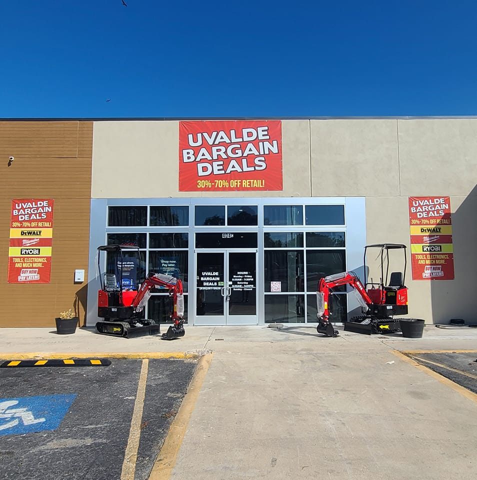 Two small red excavators sit outside a large retail store with a bright red sign advertising bargain deals in Uvalde County, Texas