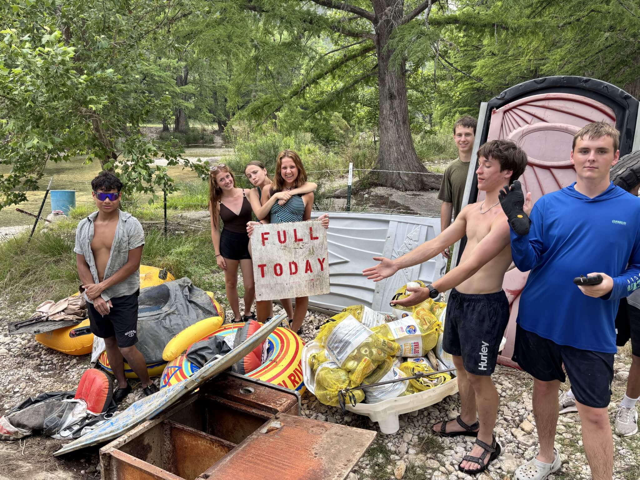 A group of students showing off the trash collected while floating the Frio Ricer, a sign being held by a young woman says "full today"