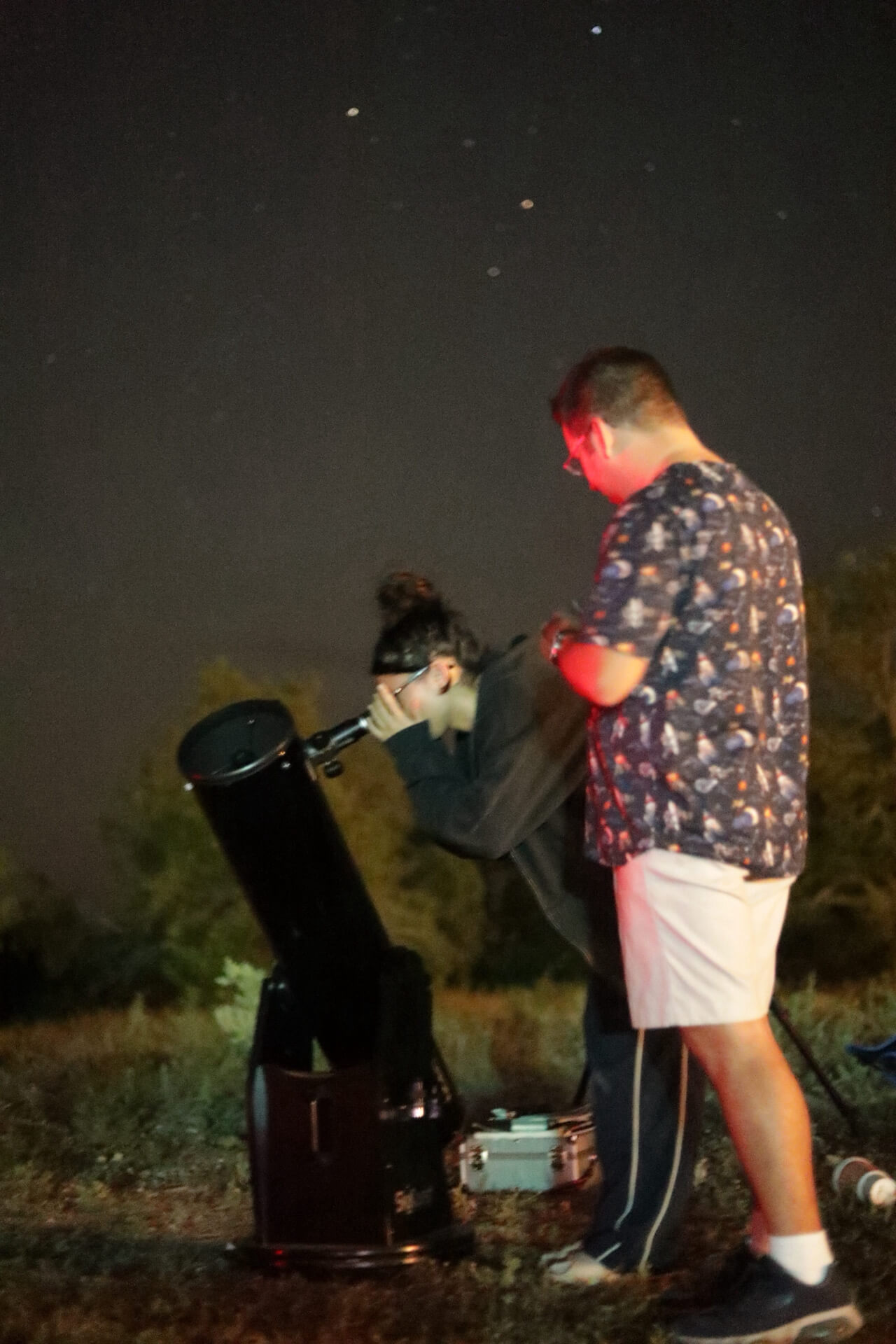 A photo of a women looking through a telescope at the stars, an astronomer stands behind her